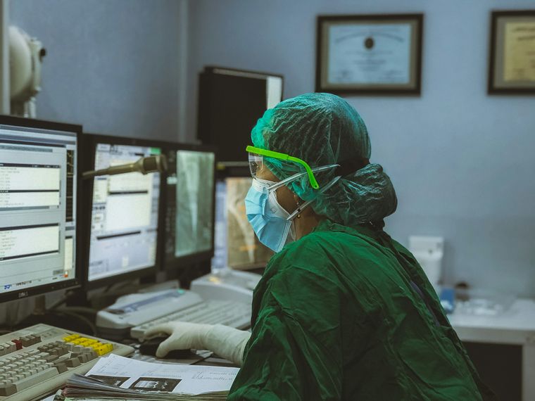 Woman in green protective clothes sitting in front of 3 computer screens holding a computer mouse